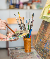 Closeup of paintbrush in little hands mixing paints on palette