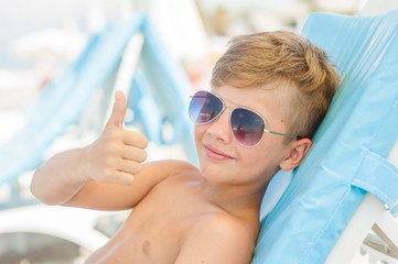 the boy on a sunny beach lies on a sun lounger in sunglasses and showing thumbs up © Ermolaev Alexandr