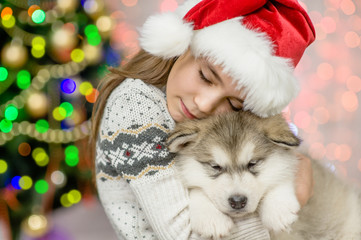 Happy girl in red santa hat hugging puppy on a background of the Christmas tree