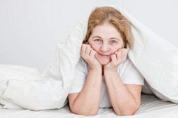 Happy senior woman lying uder blanket