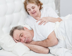 An elderly woman wakes her husband on the bed