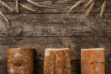 Different fresh bread and spikelets of wheat on rustic wooden background. Creative layout made of bread. Healthy food concept
