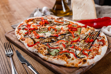 Delicious pizza with chicken, zucchini, eggplant, pepper, cheese and mushrooms on wooden rustic table. Top view. Toning