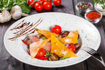 Hot salad with beef steak chargrilled to medium rare with cherry tomatoes, mushrooms and cheese on dark wooden background