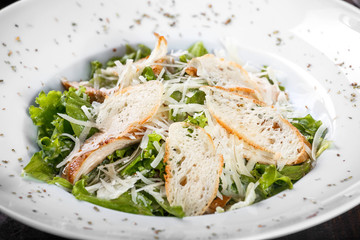 Salad with chicken breast, parmesan cheese, croutons, mixed greens, lettuce on wooden background. Healthy food