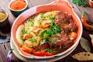 Baked meat with grilled vegetables, potatoes, greens in plate on wooden background. Hot Meat Dishes