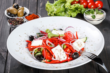 Greek salad of organic vegetables with tomatoes, cucumbers, red onion, olives, feta cheese and sweet pepper on wooden background