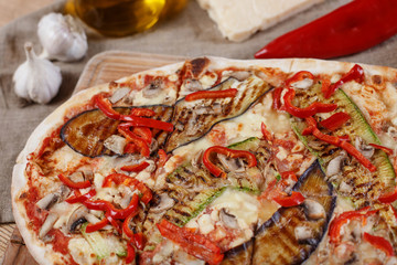 Delicious pizza with chicken, zucchini, eggplant, pepper, cheese and mushrooms on wooden rustic table. Top view. Toning