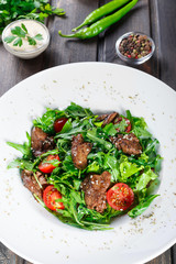 Hot salad with fried liver, cherry tomatoes and mixed greens on dark wooden background. Healthy food. Ingredients on table