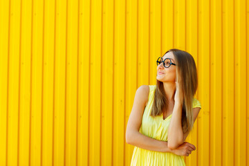 Obraz premium Portrait of a thoughtful girl wearing glasses looking up over yellow background