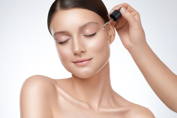 Close up women beauty portrait, one hand applying serum to her face.