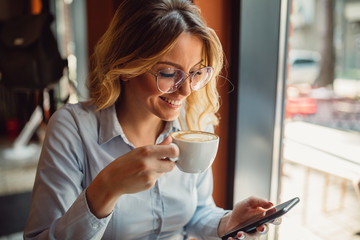 Young business woman using her smartphone in cafe during coffee break