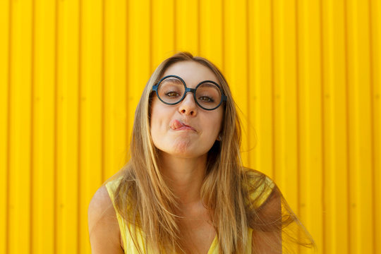 Portrait of a joyful girl wearing toy funny glasses looking up over yellow background at daylight