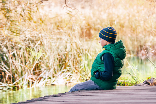 Boy sits on wooden bridge near the autumn pond