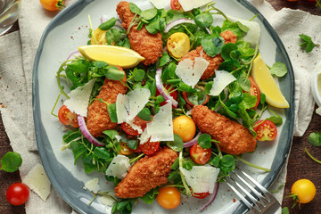 Fresh salad with chicken nuggets, cherry tomatoes, goat cheese and green vegetables in a rustic...