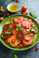 Colorful Tomato Salad with heirloom, pear shaped, beef heart, tigerella, brandywine, cherry, black tomatoes in a green plate. healthy food