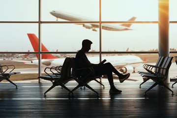 Young man sitting at airport and reding his book while waiting landing.