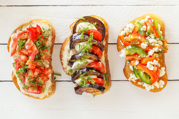 Bruschetta with fresh tomatoes and cheese, eggplant and mozzarella, sweet pepper and goat cheese on white boards. Top view.