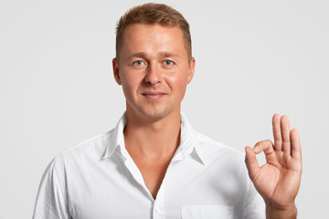 Satisfied self assured handsome man with confident expression, makes okay gesture, shows his...