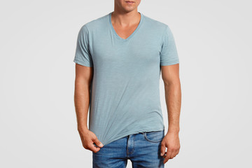 Cropped shot of muscular male in casual t shirt and jeans, stands against white background, shows blank space for your advertisement or promotional content. People, clothing and design concept