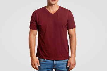 Obraz premium Indoor cropped image of muscular young man in red t shirt and jeans, stands against white background, poses over white background, blank space or your logo or advertisement. Clothing concept