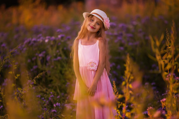 Portrait of cute young girl with long hair in a hat at sunset in the field