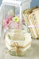 Glass jar with candle inside decorated with lace and string.