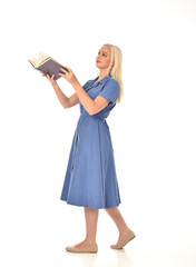 full length portrait of blonde girl wearing blue dress. standing pose holding a book. isolated on...