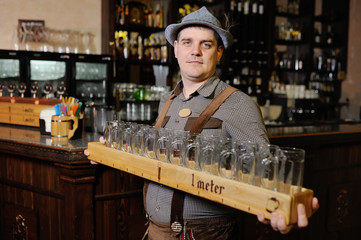 a man at the Oktoberfest festival in traditional Bavarian clothes and a hat holds a meter of beer and smiles