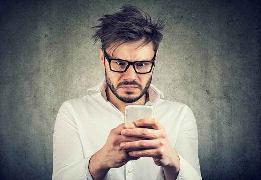 stunned man, surprised offended, by what he sees on his smartphone