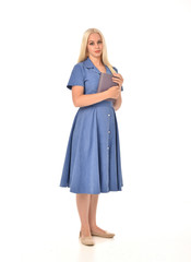 full length portrait of blonde girl wearing blue dress. standing pose holding a book. isolated on white  studio background.
