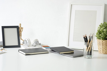 Artist workplace table with jar of pencil, sketch book, photo frame and plant decoration on white table.