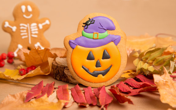 Halloween traditional sweets. Gingerbread pumpkin with a smile and skeleton on the background of autumn leaves and kraft paper. Background image for inserting text.