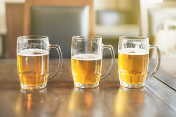 three glass mugs with beer on a wooden table in the cafe