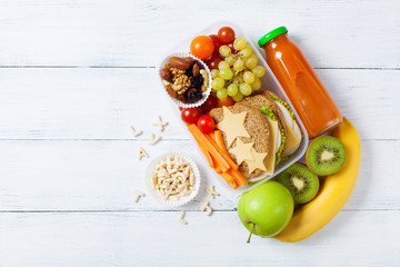 School lunch box with vegetables, fruits and sandwich for healthy snack on white wooden table top view.