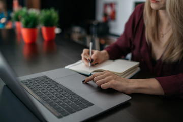 Female designer using laptop, sketching at blank notepad. Woman hand writing in notebook on wooden desk. Concept ease of use of Internet and accessibility of information of working process.