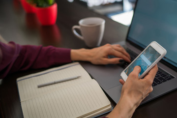 Selective focus on smartphone device which female person hold front open laptop computer sitting at...