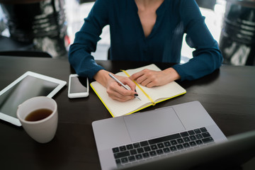 Cropped view of female student writing notes in notebook while searching useful information in...