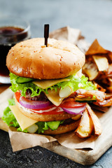 Tasty grilled beef burger with bacon, pickled onion and french fries served on a rustic wooden board on dark slate background