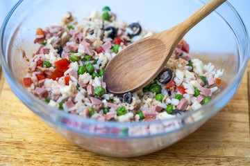 Italian rice salad or cold rice in a glass case with woodden spoon on a chopping board with white background.