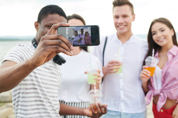 African young man photographing his friends and himself on his smartphone outdoors