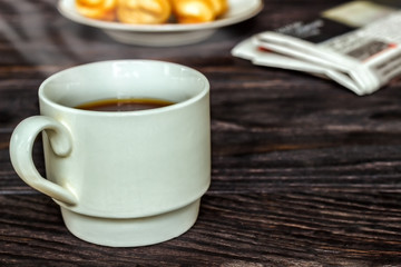 White cup with coffee and croissants on a wooden background, selective focus. The concept of breakfast.