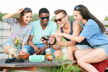 Group of young people looking photos on digital camera together and laughing during party