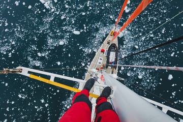 sailing boat in Antarctica, extreme dangerous  travel selfie, person feet standing on mast of a...