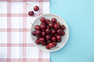 Fresh sweet cherries bowl, napkin on blue background