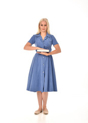full length portrait of blonde girl wearing blue dress. standing pose holding a book. isolated on white  studio background.