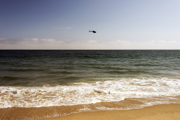 A black helicopter flying over the Pacific Ocean in Malibu beach, California in summer time