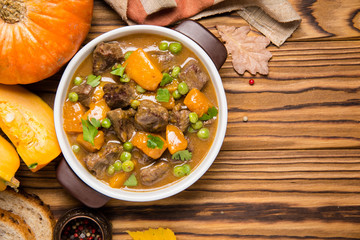 Beef stew with pumpkin, peas and thick sauce, autumn food. Dark bowl on wooden background in rustic style
