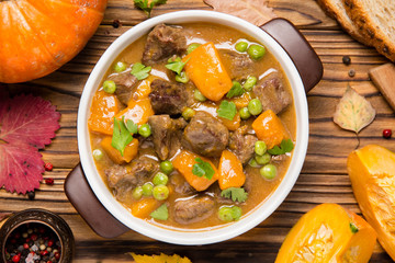 Beef stew with pumpkin, peas and thick sauce, autumn food. Dark bowl on wooden background in rustic style