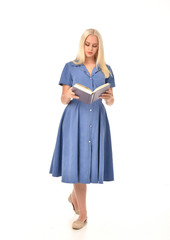 full length portrait of blonde girl wearing blue dress. standing pose holding a book. isolated on white  studio background.